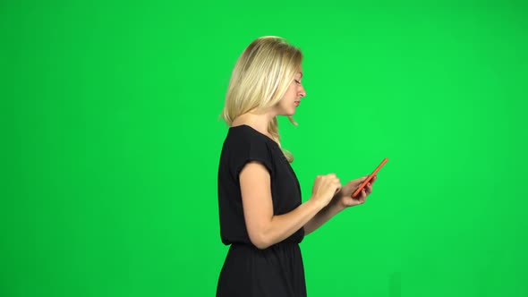 Smiling Woman Goes and Texting with Smartphone on Green Screen at Studio. Side View