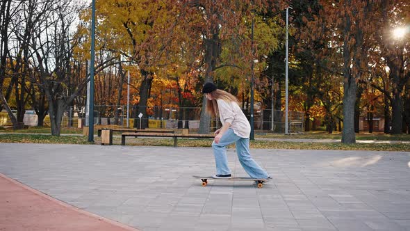 Side View of a Student Riding Fast a Skateboard in the Autumn Park and Demonstrating Tricks