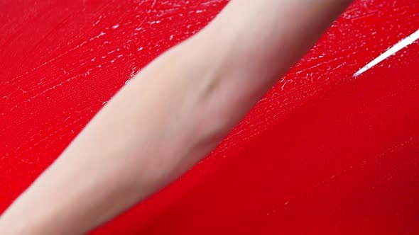 Car Washing Service  Man Wipes Water From a Red Car Surface with Rag
