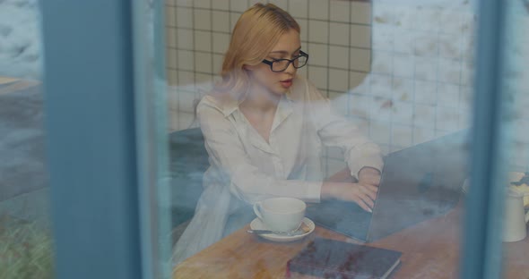 Attractive Woman in Eyeglasses Sitting with Laptop in Office or Cafe