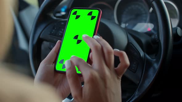 Close-up of a Woman's Hand with a Green Phone Screen on the Steering Wheel of a Car. A Young Driver