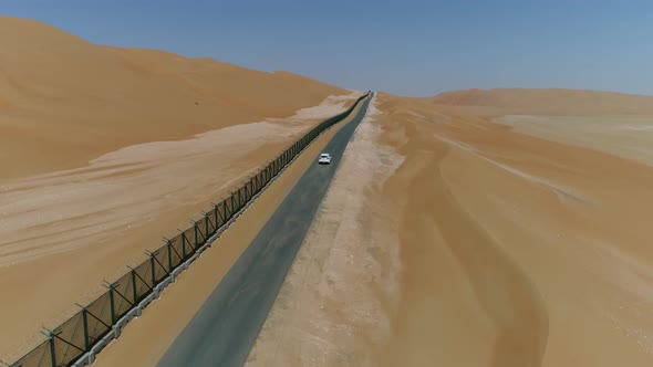 Aerial view of white car driving next to metal in the desert, Abu Dhabi.