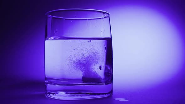 An Effervescent Soluble Tablet Falls Into a Glass of Water. On a Blue Background
