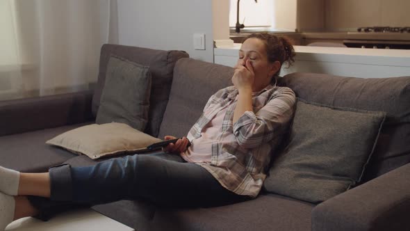 Adult Woman Holding Remote Control Watching Tv Yawning at Home