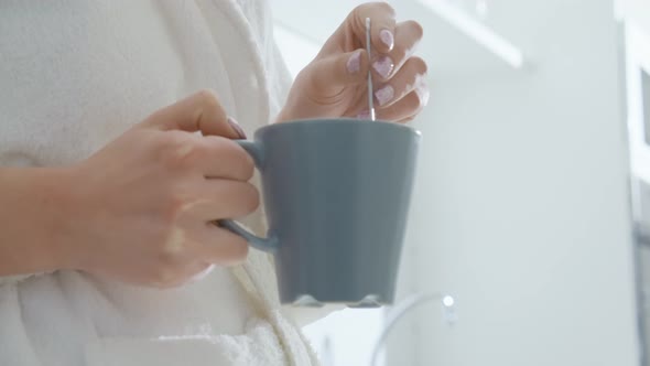 Woman Holding Grey Cup in Hands and Stirring with Spoon