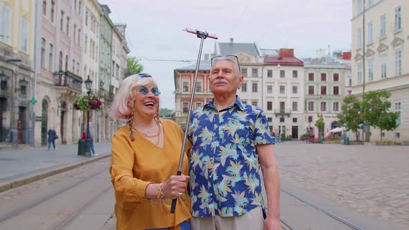 Senior Old Tourists Man with Woman Walking in City with Smartphone on Selfie Stick and Taking Photos