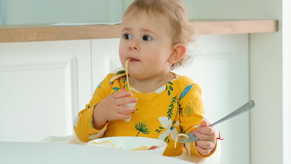 The Child Eats Spaghetti in the Kitchen