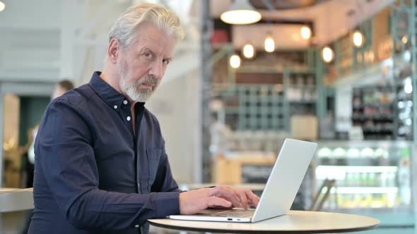 Old Man with Laptop Looking at Camera in Cafe