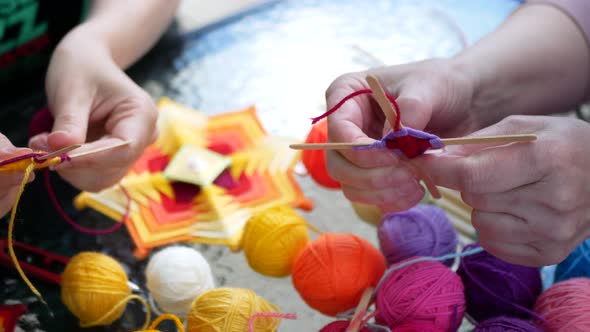Making mandalas from yarn and sticks. Women are weaving handmade 4-ray mandalas