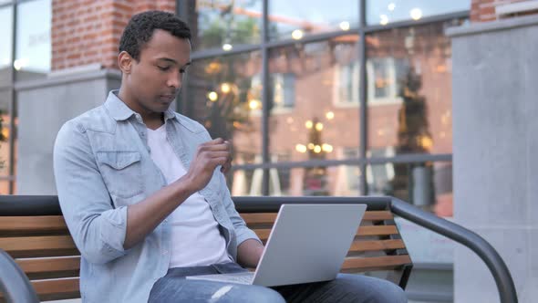 Pensive African Man working on Laptop, Sitting on Bench