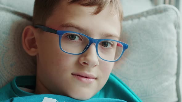 Portrait of a Male Child in Eyeglasses and Green Tshirt Laying on a Couch