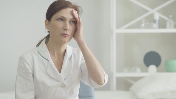 Portrait of Stressed Doctor with Headache Holding Temples with Hands and Sighing. Tired Caucasian