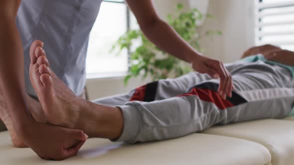 Mixed race female physiotherapist helping senior man stretching his legs