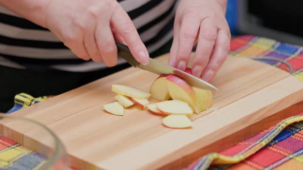 Senior Woman Cut Red Apple with a Knife on Wooden Cutting Board on a Kitchen Table