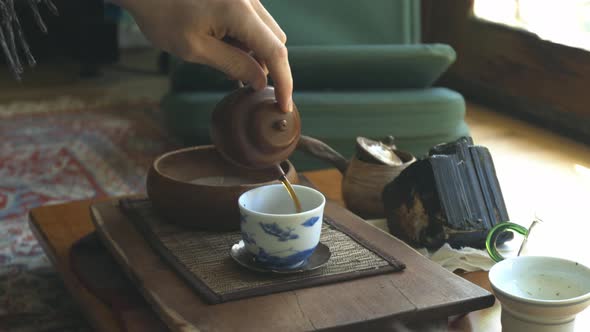 Tea being poured from an authentic clay tea pot into a white and blue cup on a tea table in ambient