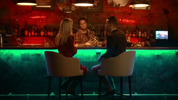 A Bewitching Couple Having a Date in the Bar - Bartender Standing and Rubs the Glass and Talking