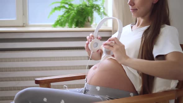 Pregnant Woman Put Headphones on Belly in Armchair