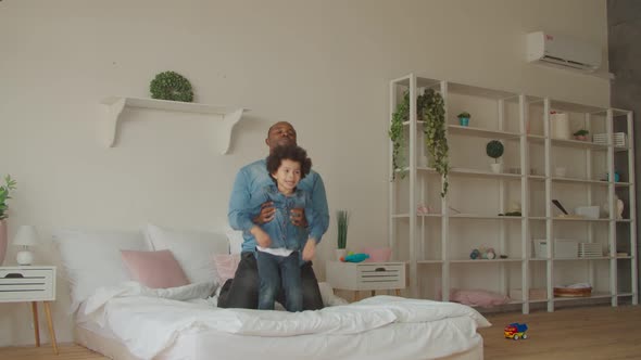 Joyful Black Father and Little Son Jumping on Bed alt