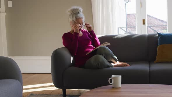 Senior caucasian woman reading a book while sitting on the couch at home