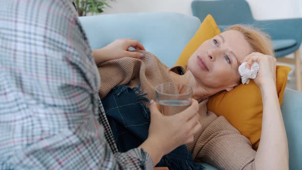 Unhealthy Mature Woman Lying on Sofa When Daughter Bringing Her Water and Medication Caring for Mom