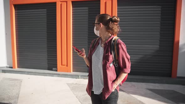 A Young Woman in a Protective Medical Mask and Glasses Using Her Smartphone