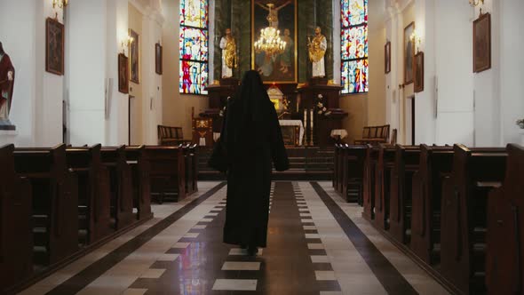 Nun walking inside a catholic church toward the sacred altar seen from behind, religious people conc