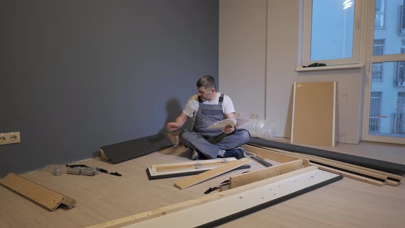 A Builder in a Work Overalls is Assembling a Bed in a New Apartment