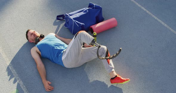 Caucasian disabled male athlete with running blade wearing headphones and stretching