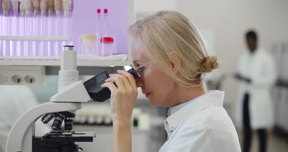 Caucasian Mature Female Scientist Looking Under Microscope Analyzing Sample