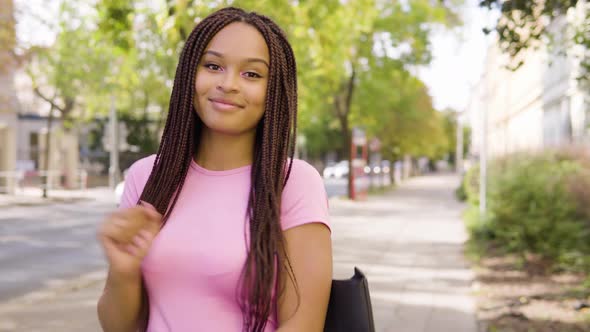 A Young Black Woman Dances and Smiles at the Camera in the Street in an Urban Area