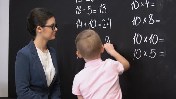 Smart Schoolboy Solving Math Exercises on Blackboard, Teacher Standing Near