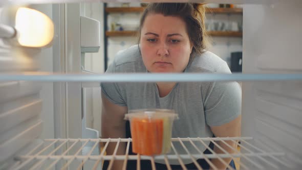 Overweight Woman on Diet Opening Empty Fridge with Only Container with Vegetables and Taking It