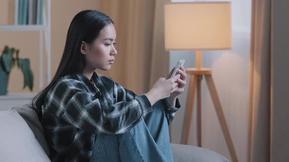 Side View of Sad Bored Asian Woman Girl Sitting on Sofa at Home with Telephone Serious Unhappy Lady