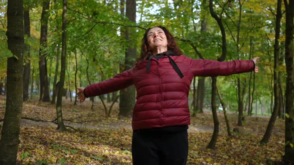 Portrait of Happy Mature Woman Stretching Hands Spinning Looking Up Standing in Autumn Forest