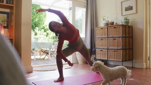 Smiling caucasian woman practicing yoga with her pet dog at home