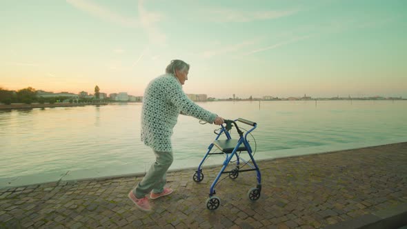 Old Woman Walks Along Road with Rollator Near Venice Lagoon