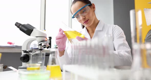 Woman Technologist in the Laboratory Looks at Liquid in Flask