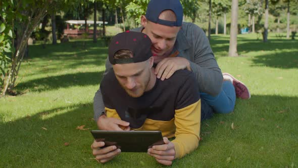 Homosexual Partners with Tablet Pc Lying on Lawn