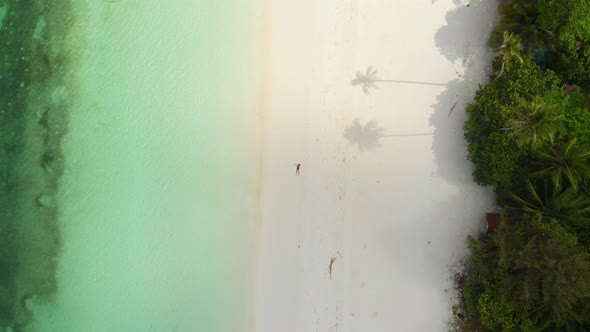 Aerial: Woman relaxing on white sand beach turquoise water tropical coastline Pa