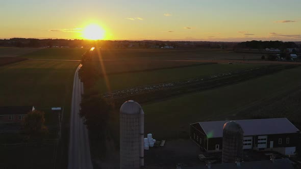 Reverse drone shot that reveals a farmhouse and grain silos during a surreal sunset