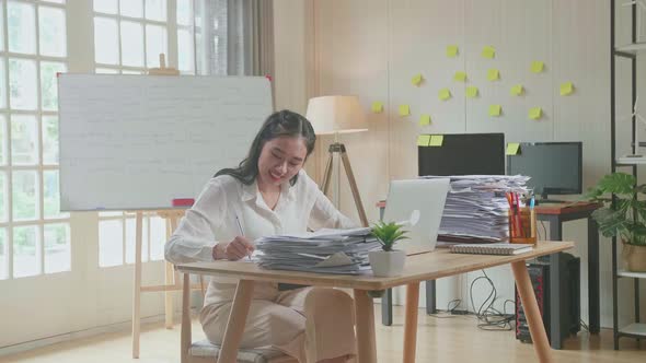 Asian Woman Looking At Laptop And Taking Note While Working With Documents At The Office