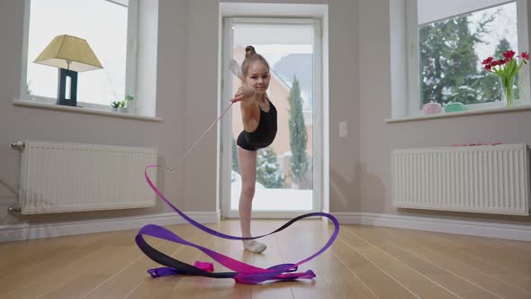 Slim Teen Girl Standing on One Leg Twirling Gymnastic Ribbon in Slow Motion