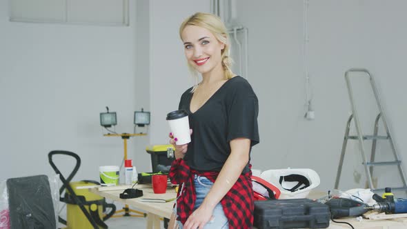 Smiling Female with Paper Cup in Workshop