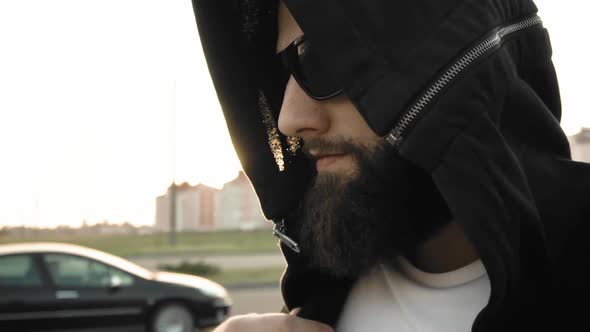 Portrait of Bearded Guy in Black Glasses and Hood. Brutal Stylish Man with Rings and Signet on