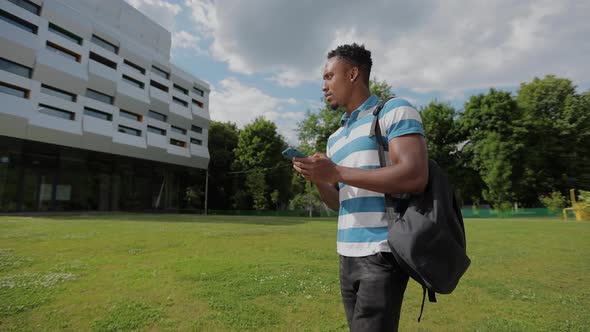 Handsome Afroamerican Man Using Smartphone on the Background of the University