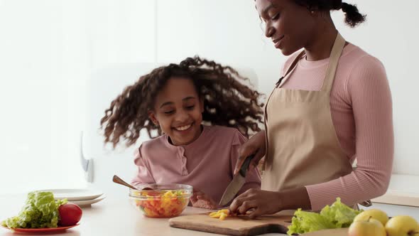 Young African American Mother Preparing Vegetable Salad Curly Little Daughter Coming and Eating