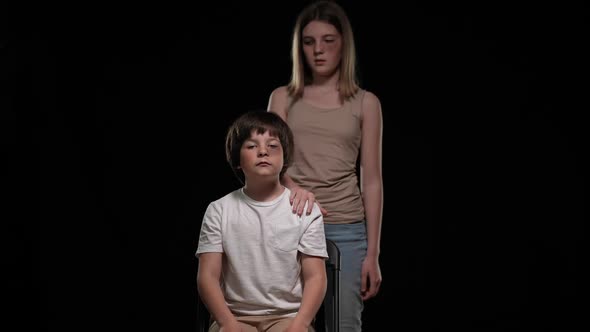 Unhappy Bruised Abused Boy Sitting on Chair Touching Girl Hand on Shoulder Looking at Camera