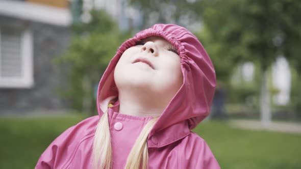Close-up Portrait of Nice Positive Little Girl in Pink Hood Looking Up and Talking. Joyful Beautiful