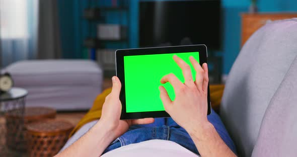 Young Man Using with Green Mockup Screen Tablet Computer in Horizontal Landscape Mode