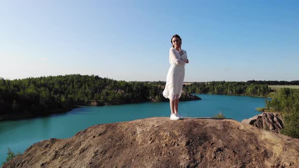 Beautiful Slender Hot Woman Bride in White Dress Stands on Peak of Mountain and Poses